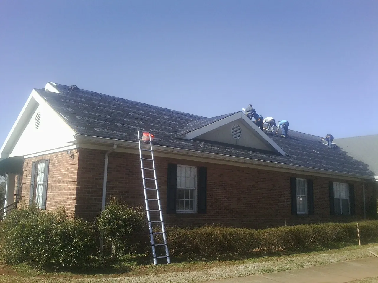 Crew tearing shingles off a brick ranch roof with a ladder set — Emergency Roof Repair work by our crew in Succasunna