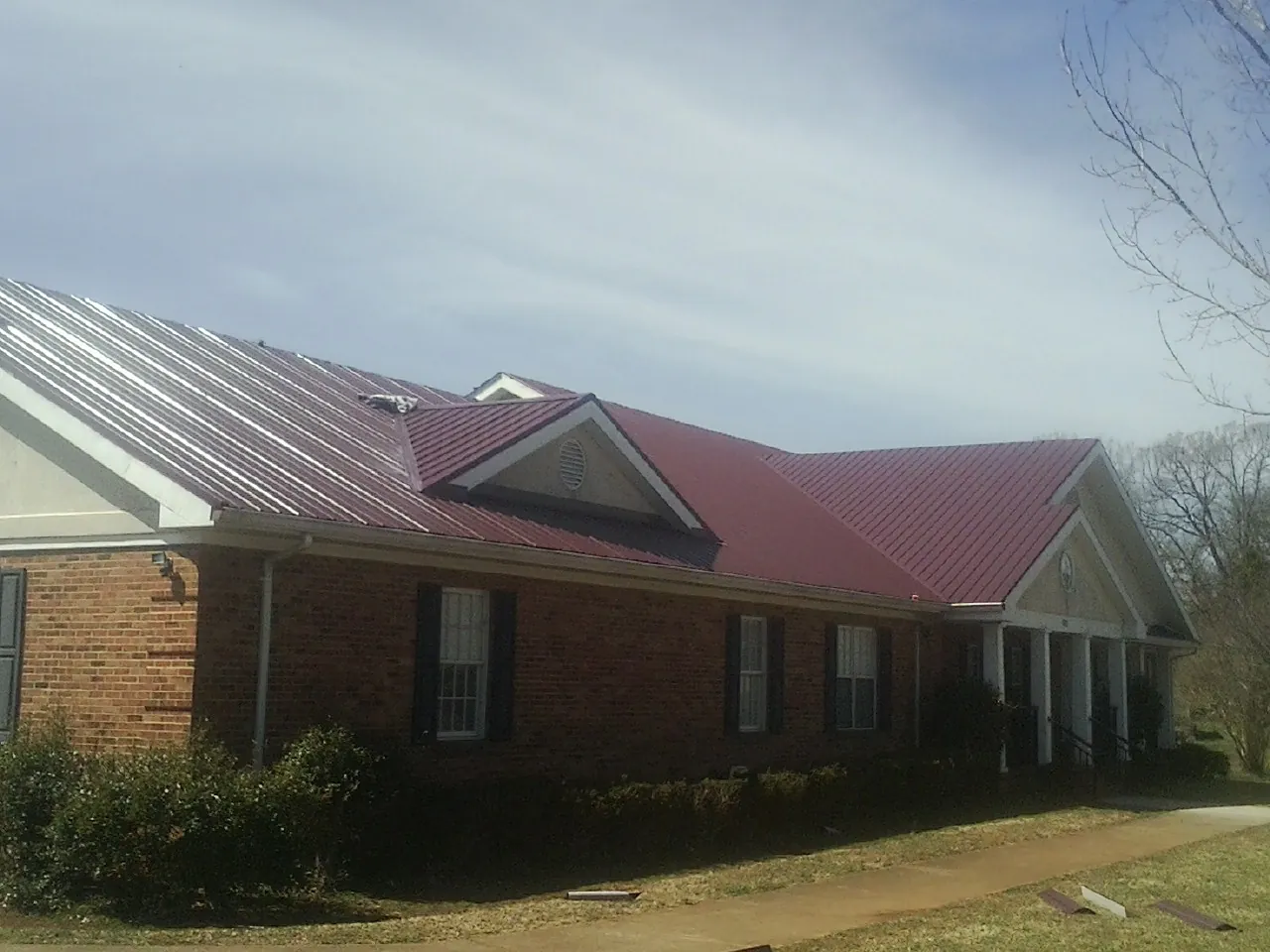 Red metal roof with gabled entries on a long brick building, from a Hail Damage Roof Repair job in Succasunna