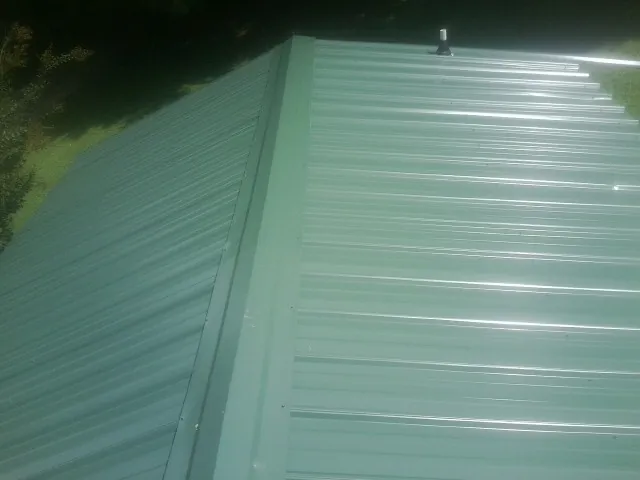 New green metal panels meeting at the ridge of a roof — Flat Roof Repair work by our crew in Succasunna
