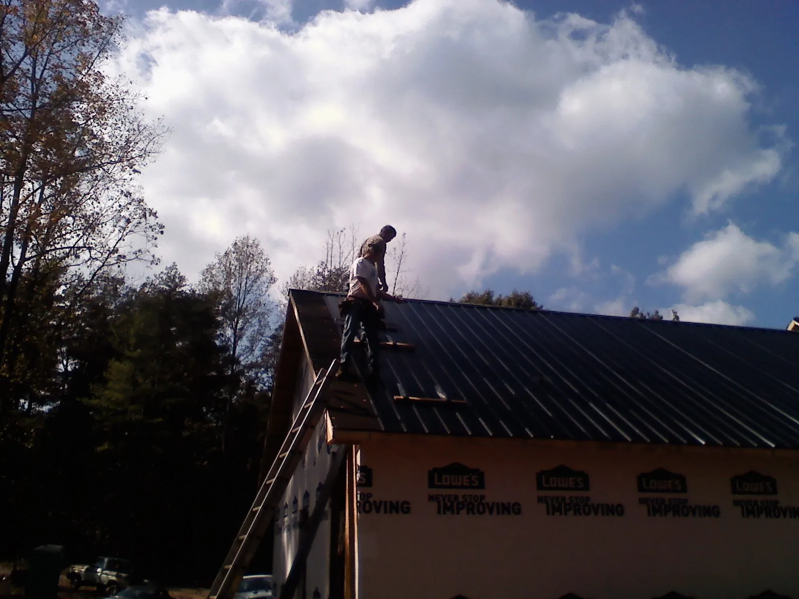 Roofer fastening dark metal panels high against a cloudy sky, from a Roof Inspection job in Succasunna