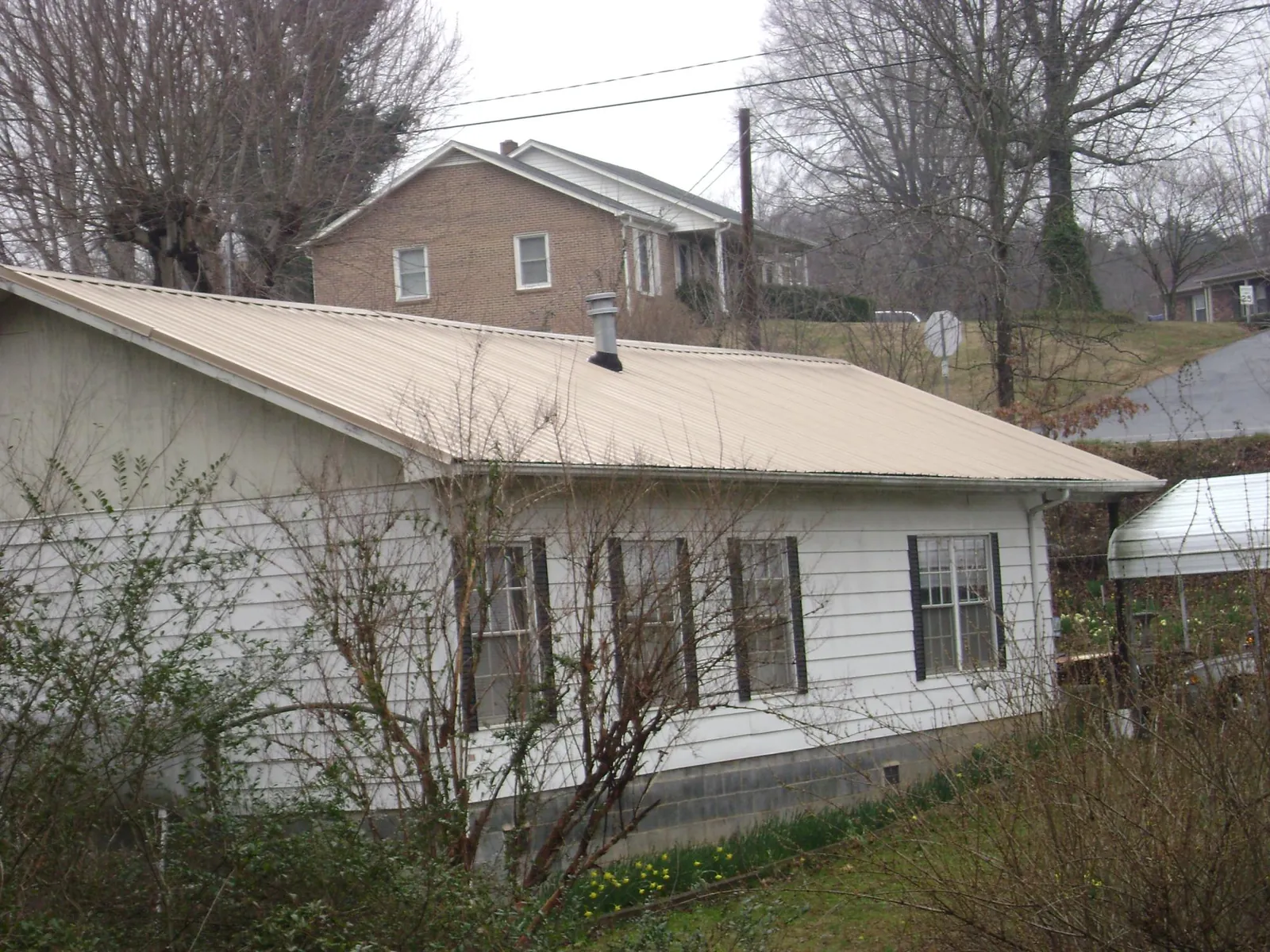 Tan metal roof on a white sided house set into a hillside — Commercial Roofing by Roofing Brothers in Succasunna